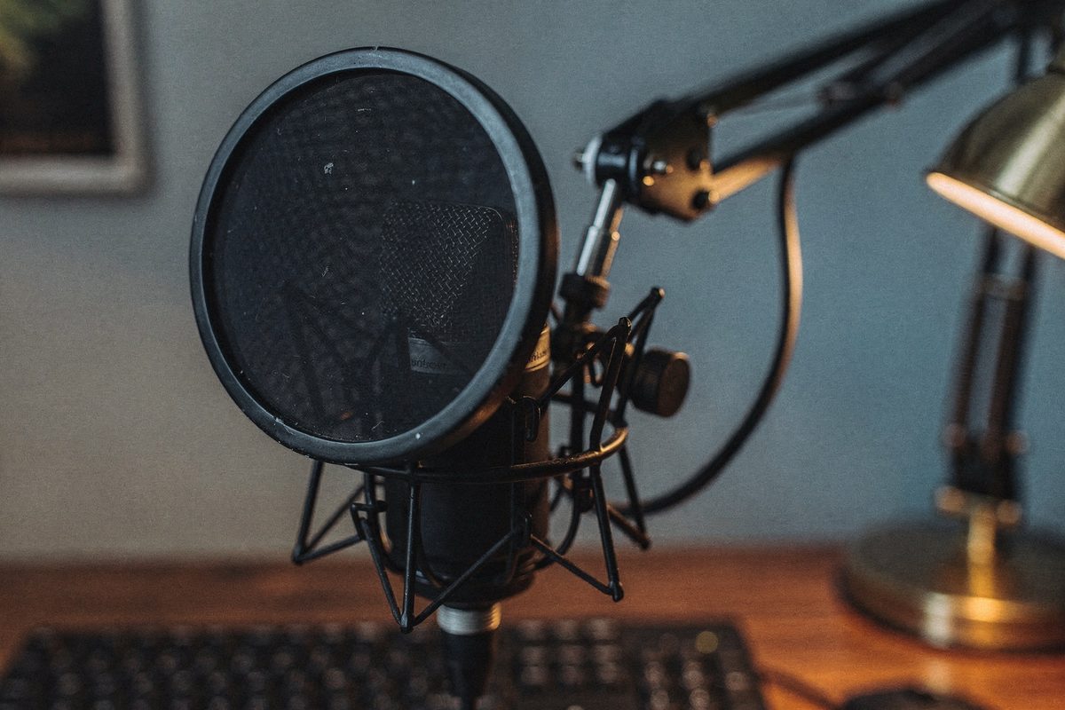 A studio condenser microphone on a boom arm with a pop filter above a desk